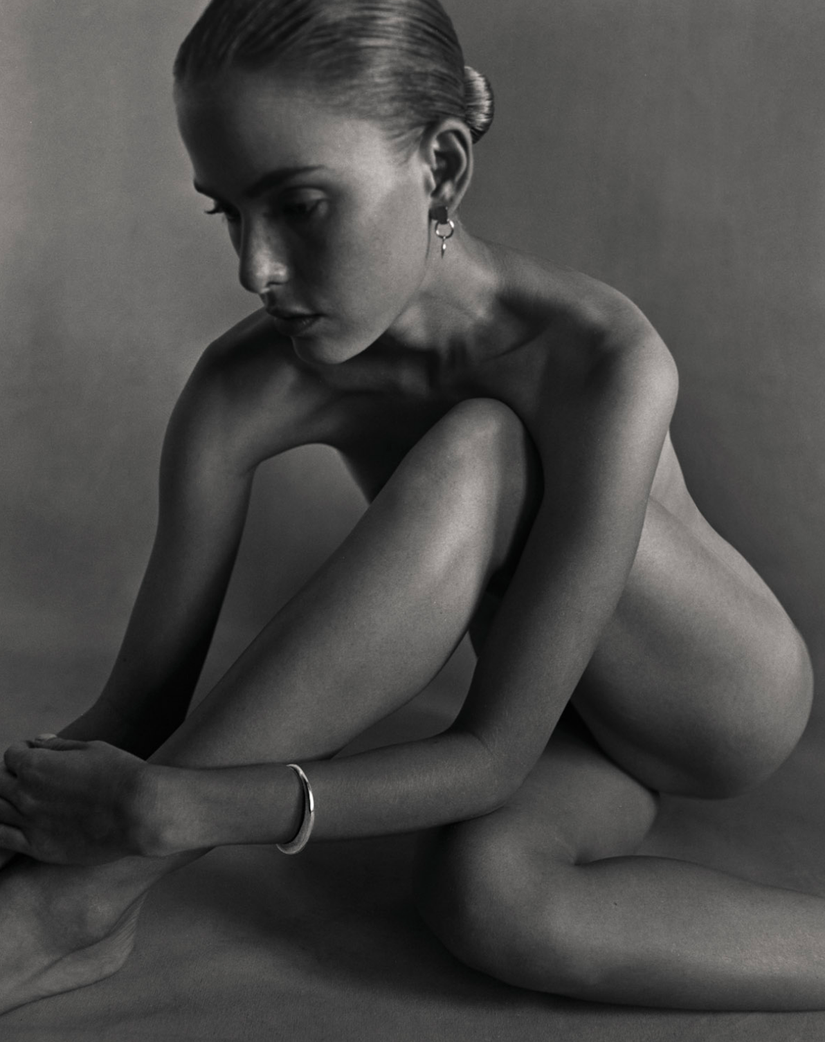 Black and white image of i seira model wearing nothing but the open bangle and the geometric pod earrings