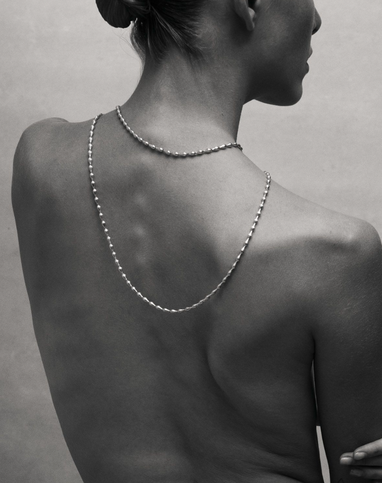 Black and white image of i seira model with the layered pod necklace across her back