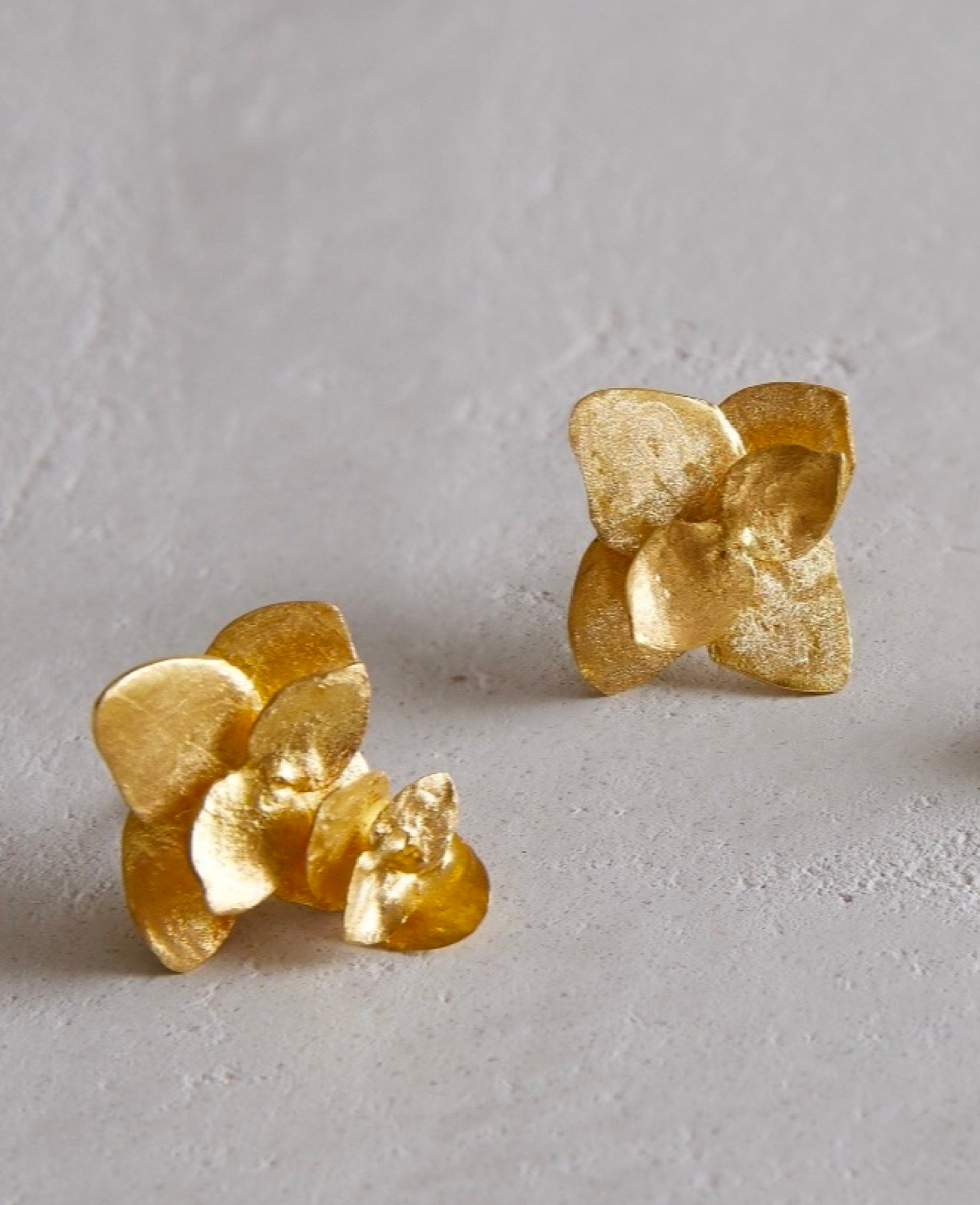 Close up images of original i seira floral gold earrings on a concrete surface