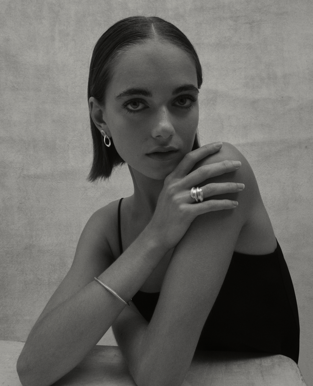 black and white image of i seira model wearing the oval bangle paired with two sculptural rings and the sculptural earrings