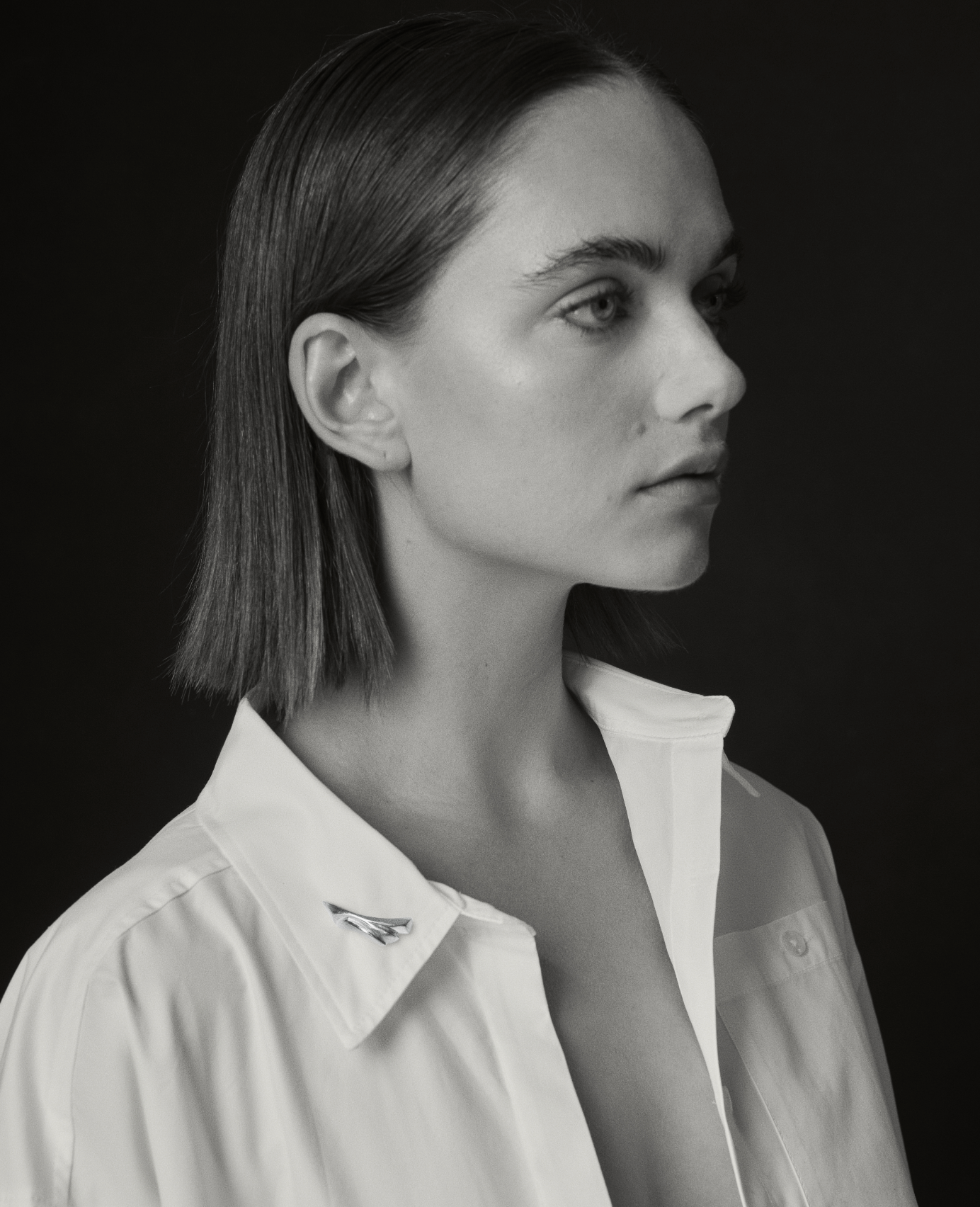 black and white image of i seira model wearing a white shirt with the sculptural gold pin on the collar