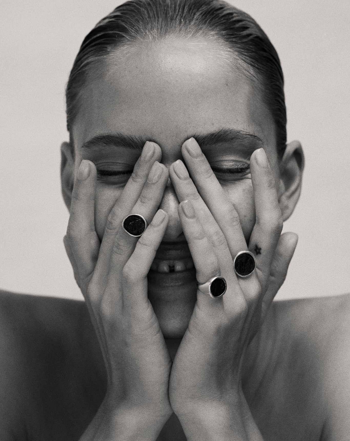 Black and white image of i seira model with her hands over her face, smiling, wearing the statement rings on three fingers