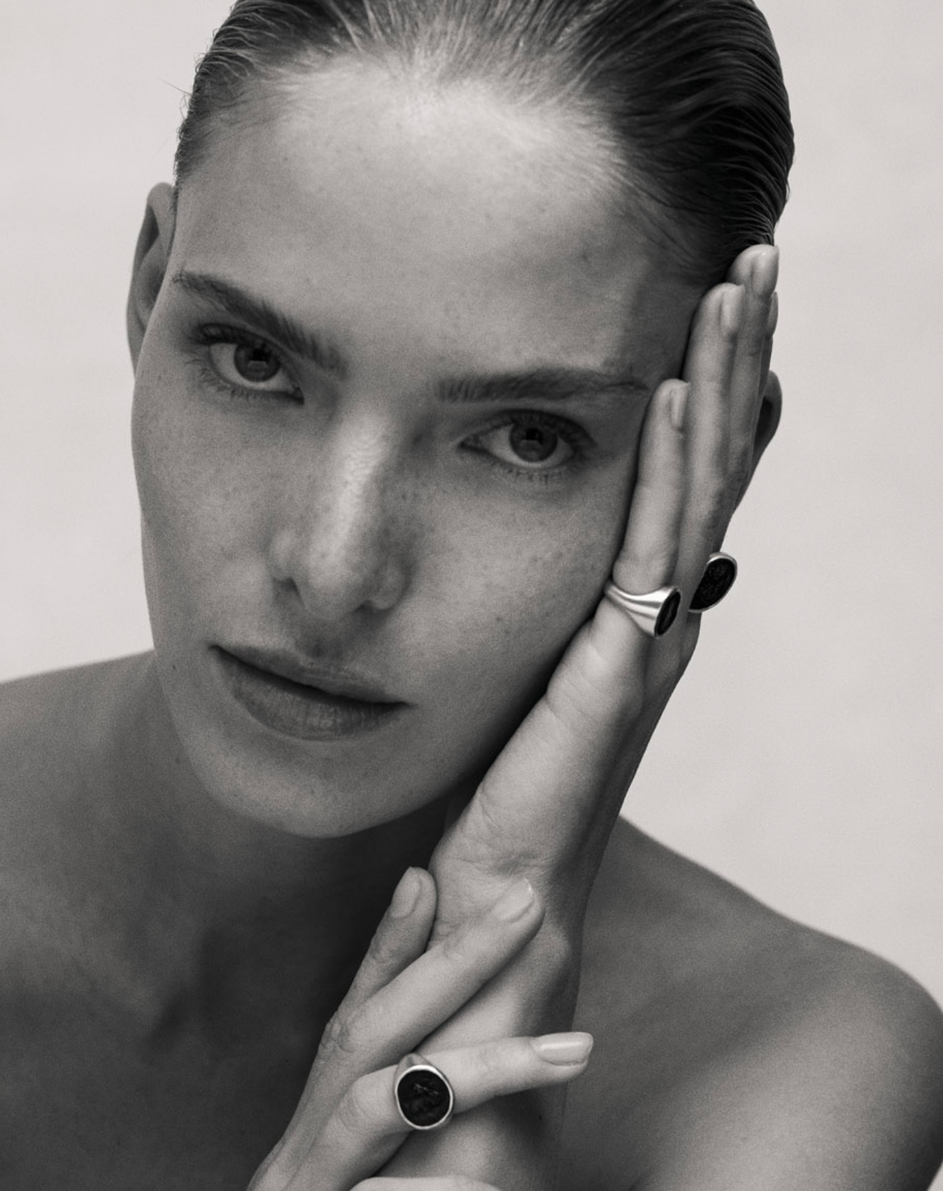 Black and white image of i seira model with her head resting on one hand, wearing the statement rings on three fingers