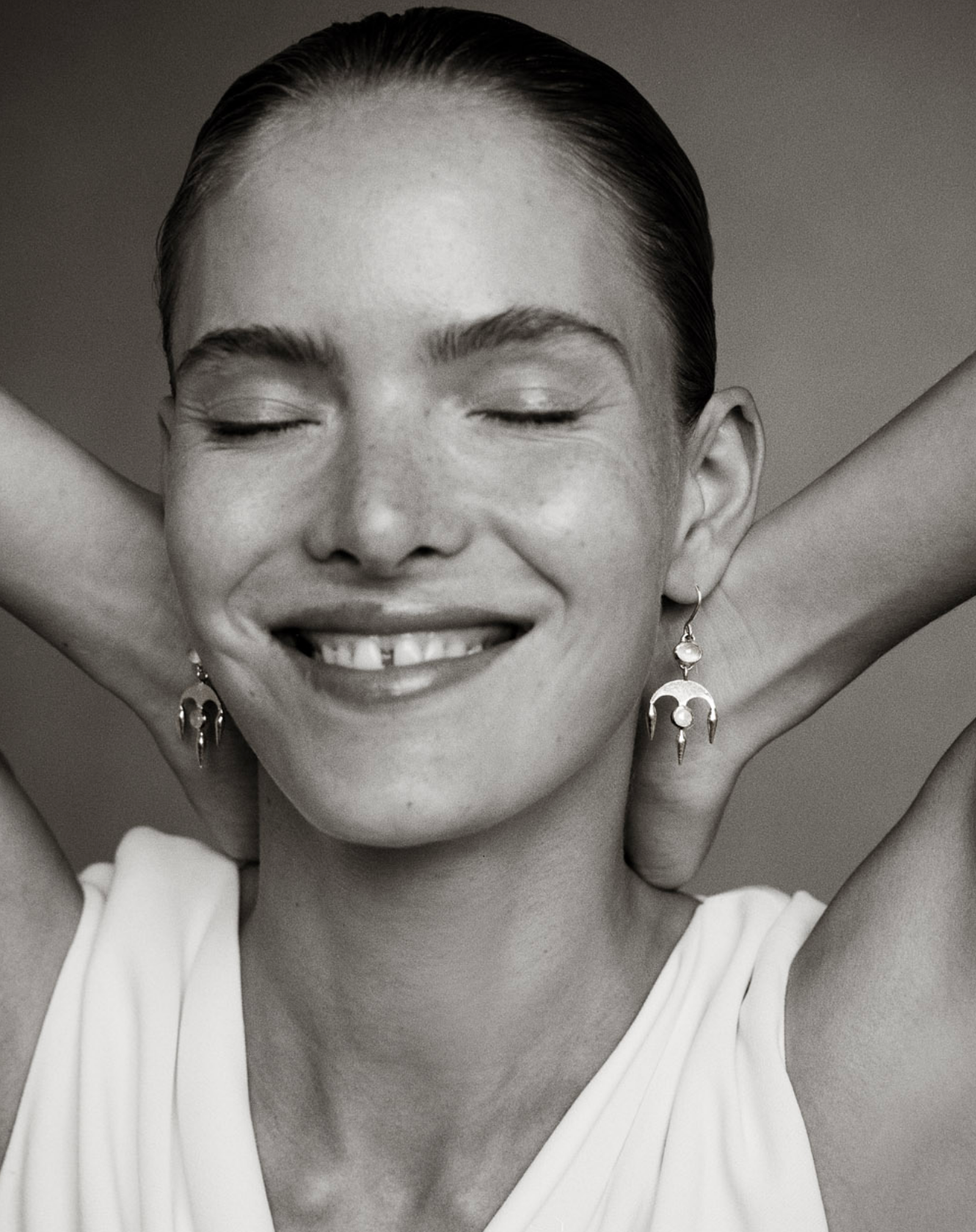 Black and white image of i seira model smiling wearing the chandelier earrings in white moonstone with her eyes closed