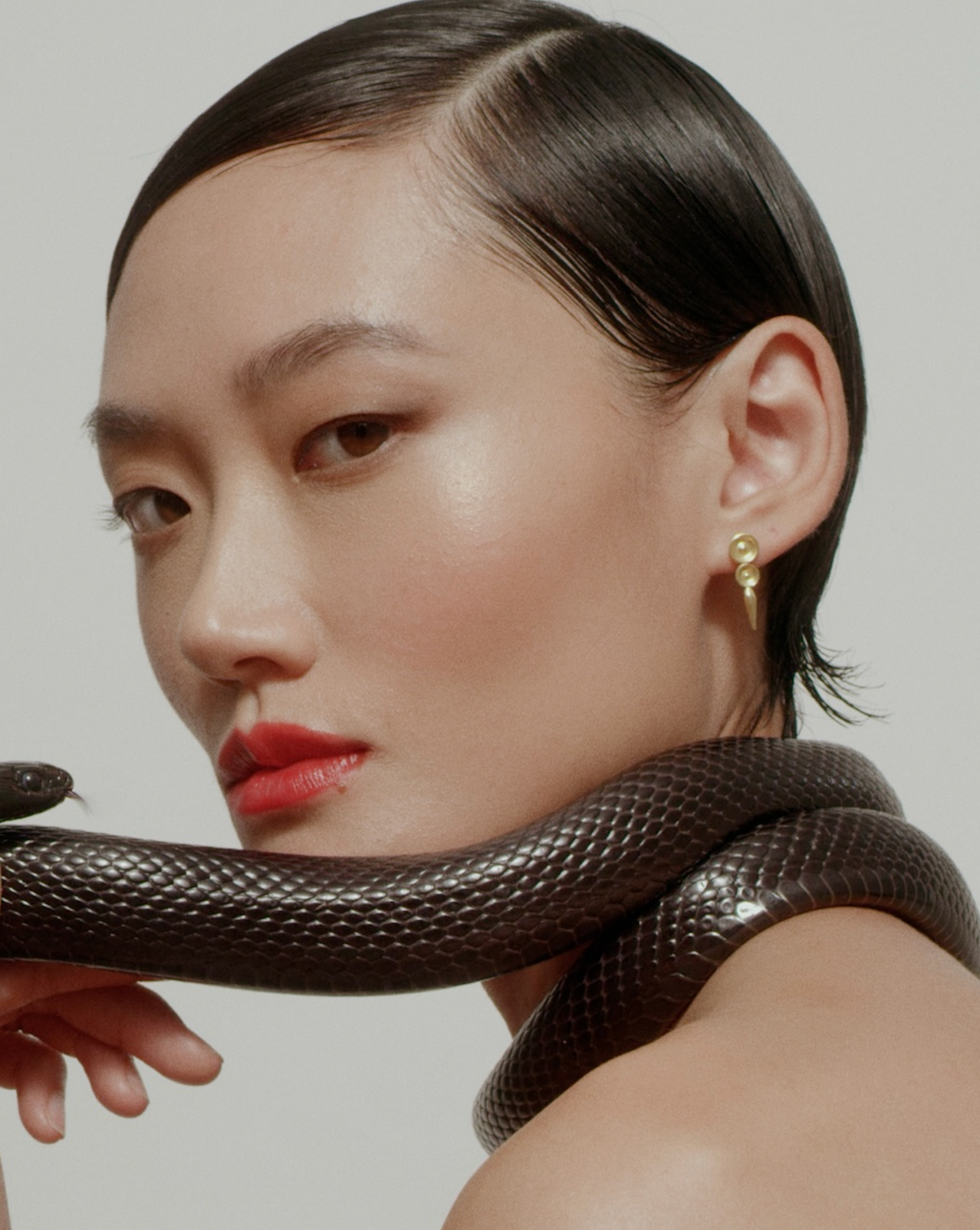 Model wears i seira gold earrings with a snake draped over her body