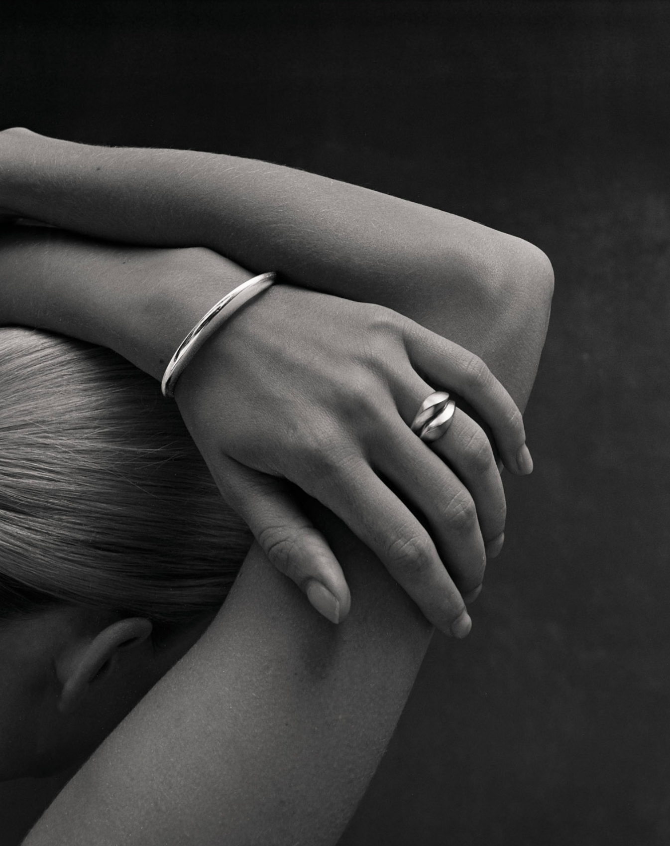 Black and white close up image of i seira model holding her arms above her head wearing the oval bangle and the sculptural rings