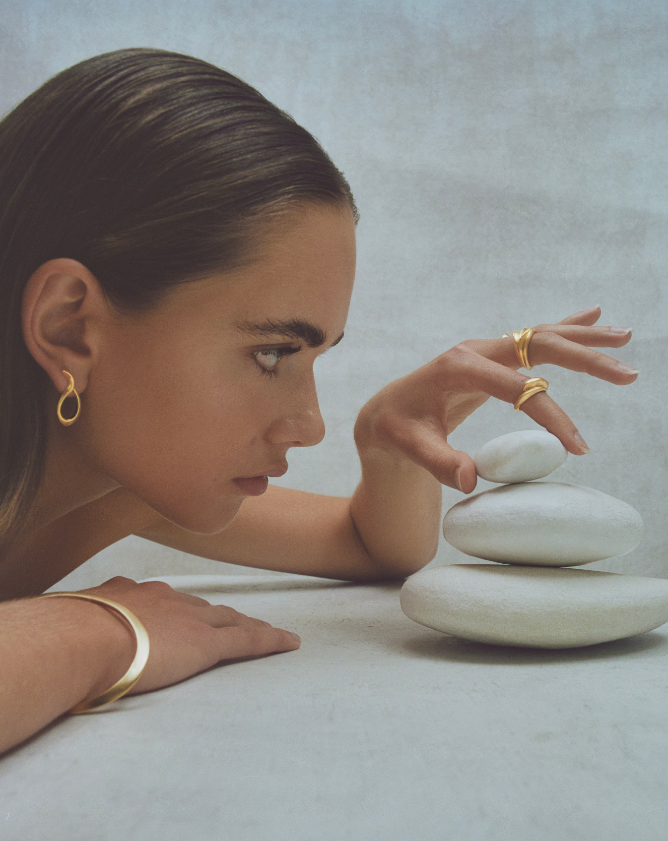 i seira model looking to the side, stacking white stones, wearing the oval bangle, sculptural rings, and sculptural earrings